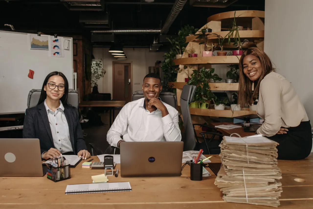Three colleagues smiling at their desks in a bright, modern office