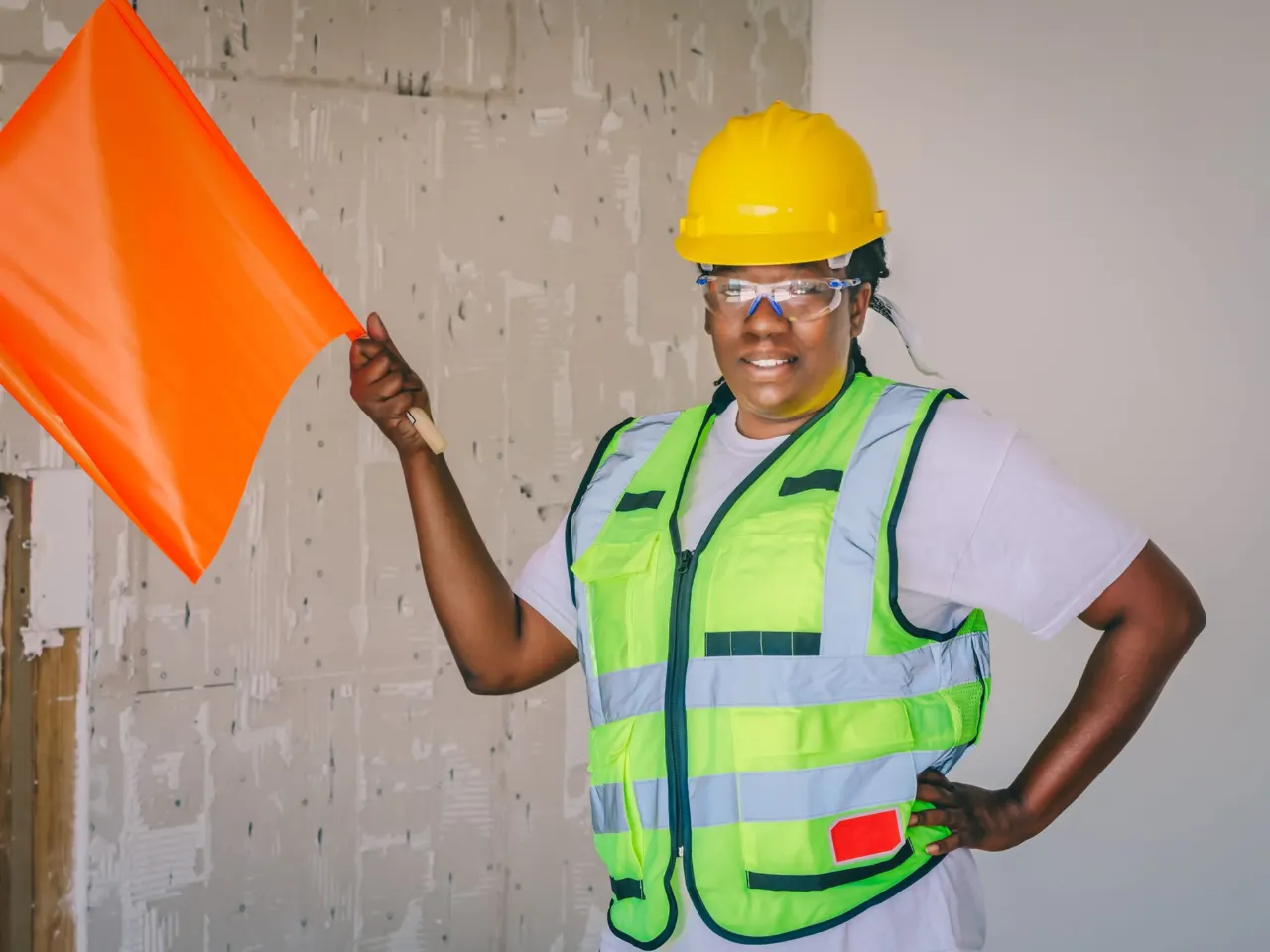 A site worker in a hard hat and high-visibility vest holding a signal flag